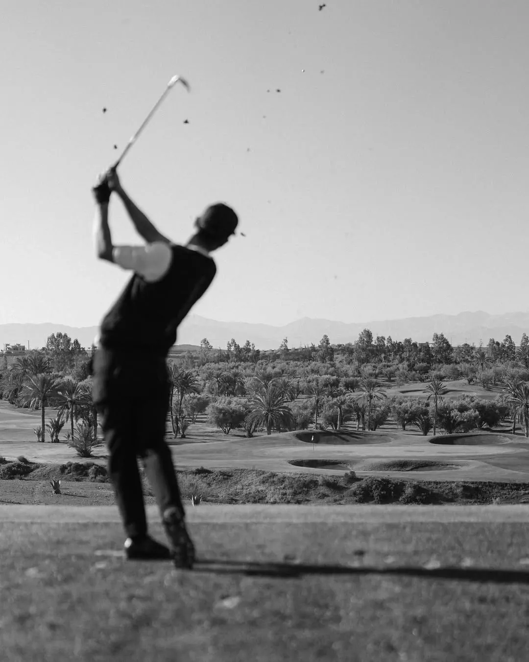 Golfer im Durchschwung, dahinter ein Grün mit Bunkern